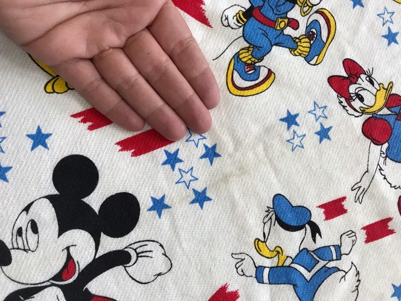 May include: White fabric with a red, white and blue pattern featuring Mickey Mouse, Donald Duck and Minnie Mouse. The fabric has a red, white and blue star pattern.