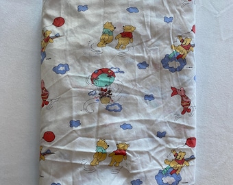 May include: White Winnie the Pooh fitted sheet with a repeating pattern of Winnie the Pooh and Piglet characters flying in hot air balloons and on clouds. The sheet has a blue and red colour scheme.