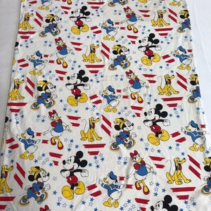 May include: A white cotton fabric with a repeating pattern of Mickey Mouse, Minnie Mouse, Donald Duck, and Pluto. The characters are wearing red, white, and blue clothing and are standing on a background of red and white stripes and blue stars.