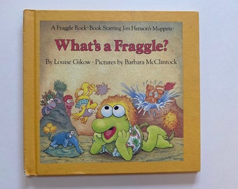 May include: A yellow book cover with the title "What's a Fraggle?"  A Fraggle Rock-Book Starring Jim Henson's Muppets. By Louise Gikow. Pictures by Barbara McClintock. The cover features a green Fraggle with orange hair and large eyes.