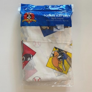 May include: A white toddler flat sheet with a Looney Tunes theme. The sheet features a repeating pattern of Bugs Bunny, Daffy Duck, Tweety Bird, and Sylvester the Cat. The sheet is packaged in a clear plastic bag with a blue header that reads "Toddler Flat Sheet Slightly Irregular 45 in. x 60 in. (114.3 cm x 152.4 cm)"