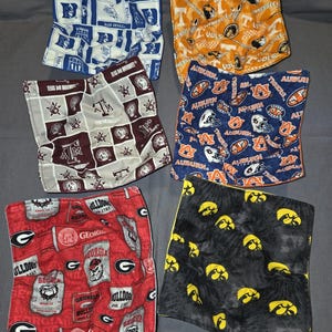 May include: Six fabric bowl cozies with various college team logos and colors. Designs include blue and white "Blue Devils", orange and white "Tennessee Vols", maroon and gray "Texas A&M", navy and orange "Auburn Tigers", red and white "Georgia Bulldogs", and black and yellow "Iowa Hawkeyes".
