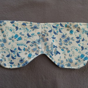 May include: A white sleep mask with a blue and white floral pattern. The mask is curved to fit over the eyes and has a seam down the center.