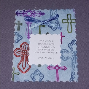 May include: A small blue fabric pouch with a white tag that reads "GOD IS OUR REFUGE AND STRENGTH; A VERY PRESENT HELP IN TROUBLE PSALM 46:1". The pouch is decorated with colorful crosses.