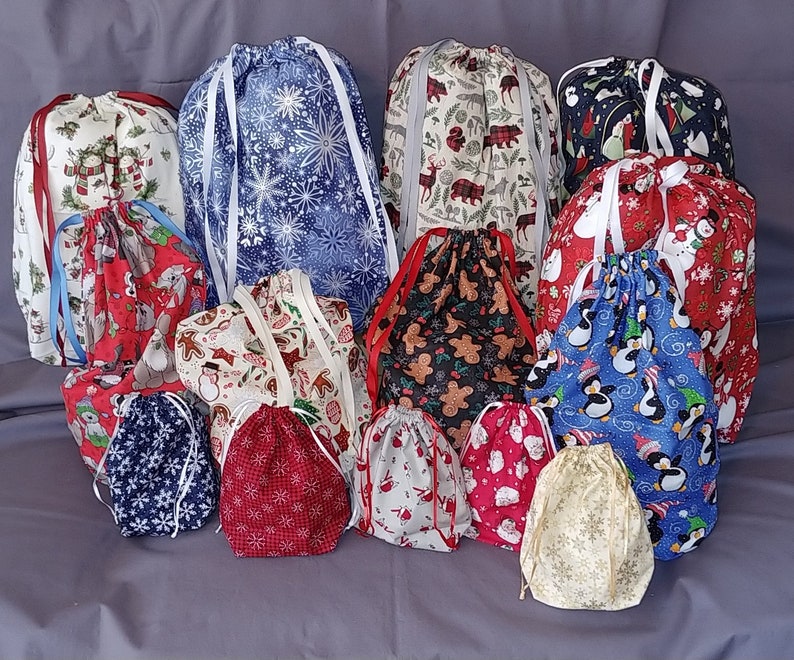 May include: A collection of 16 colorful drawstring bags with various holiday-themed patterns, including penguins, gingerbread men, snowflakes, and Christmas trees. The bags are made of fabric and have white drawstrings.