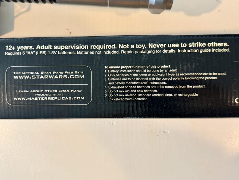 May include: Black product packaging with text including "12+ years. Adult supervision required. Not a toy." and "WWW.STARWARS.COM." Requires 6 AA batteries. Instructions included. The product is from Master Replicas.