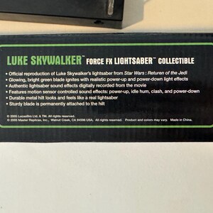 May include: A black box with green text that reads "LUKE SKYWALKER FORCE FX LIGHTSABER COLLECTIBLE." The box describes the lightsaber's features, including sound effects and a durable metal hilt. The lightsaber is from Star Wars: Return of the Jedi.