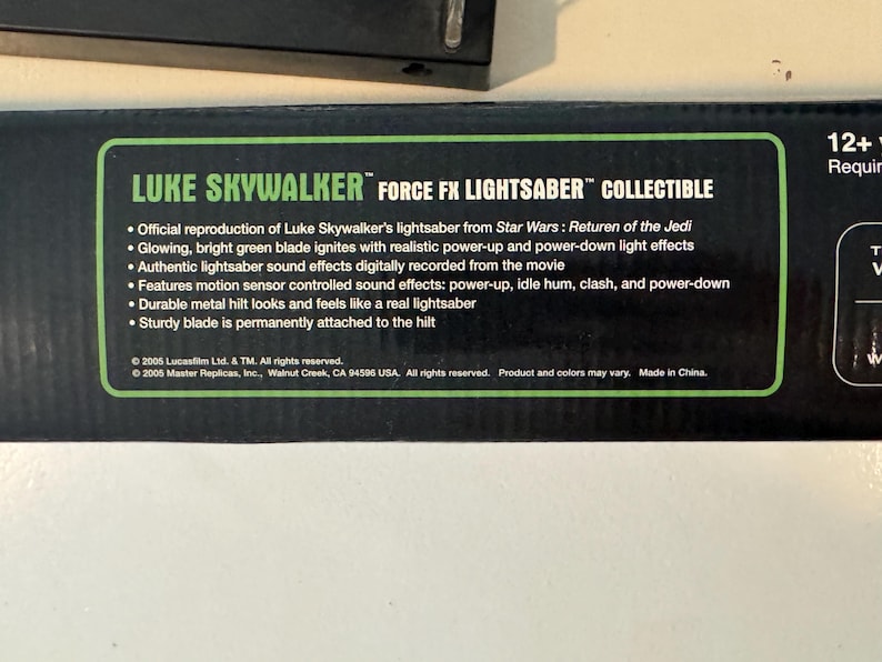 May include: A black box with green text that reads "LUKE SKYWALKER FORCE FX LIGHTSABER COLLECTIBLE." The box describes the lightsaber's features, including sound effects and a durable metal hilt. The lightsaber is from Star Wars: Return of the Jedi.