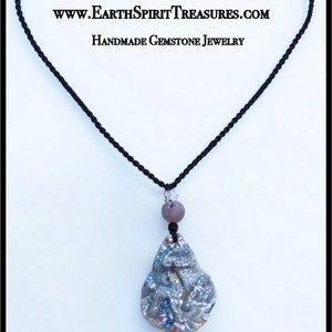 K&ouml;nnte beinhalten: Halskette mit einem handgefertigten Edelstein-Anh&auml;nger in Tropfenform mit schillernden Farben. Der Anh&auml;nger h&auml;ngt an einer schwarzen Kordel, mit einer lila Perle und einem klaren Kristall. Der Text "www.EarthSpiritTreasures.com Handmade Gemstone Jewelry" ist oben.