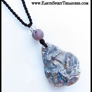 K&ouml;nnte beinhalten: Halskette mit einem gro&szlig;en, irisierenden, grau-blauen Steinanh&auml;nger und einer schwarzen Kordel. Der Anh&auml;nger ist mit einer lila Perle und einem klaren Kristall verbunden. Die Halskette wird vor wei&szlig;em Hintergrund pr&auml;sentiert. Text: www.EarthSpiritTreasures.com