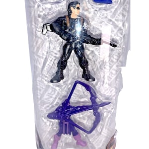 Op de afbeelding: Een plastic verpakking met een zwart action figure van een superheld die een pistool en een paarse boog met pijlen vasthoudt.