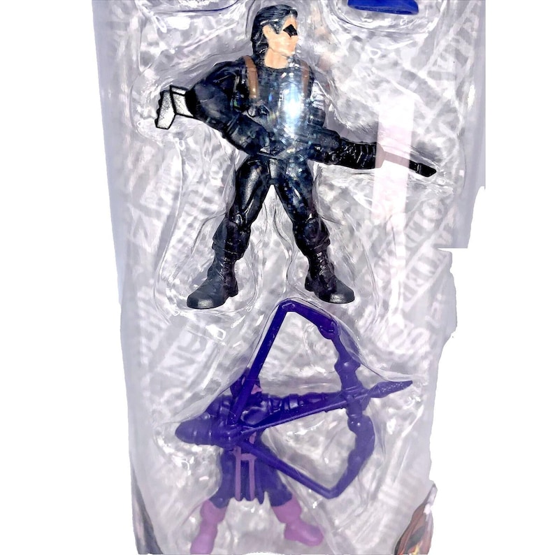 Op de afbeelding: Een plastic verpakking met een zwart action figure van een superheld die een pistool en een paarse boog met pijlen vasthoudt.