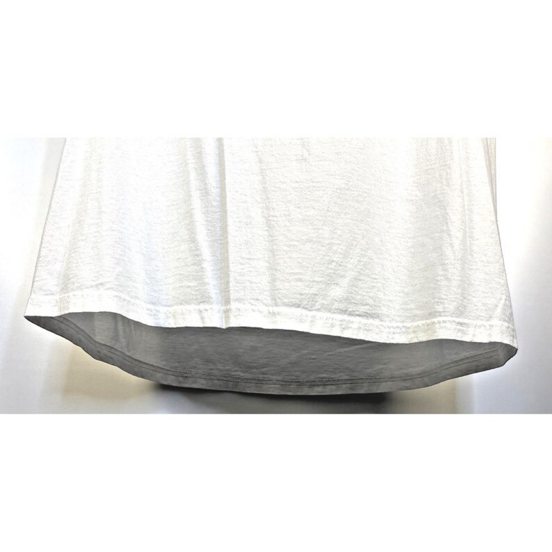 May include: A white t-shirt with a curved hemline. The fabric appears to be slightly textured, with subtle variations in tone. The bottom hem is a darker shade of gray.