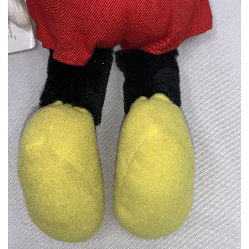 Puede incluir: Primer plano de la parte inferior de un juguete de peluche de Mickey Mouse. Los pies son amarillos y las piernas son negras.