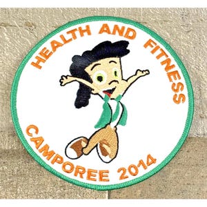 May include: Embroidered patch with a cartoon figure in a green and white outfit, arms outstretched. The patch is round with a green border and the words "HEALTH AND FITNESS CAMPOREE 2014" in orange.