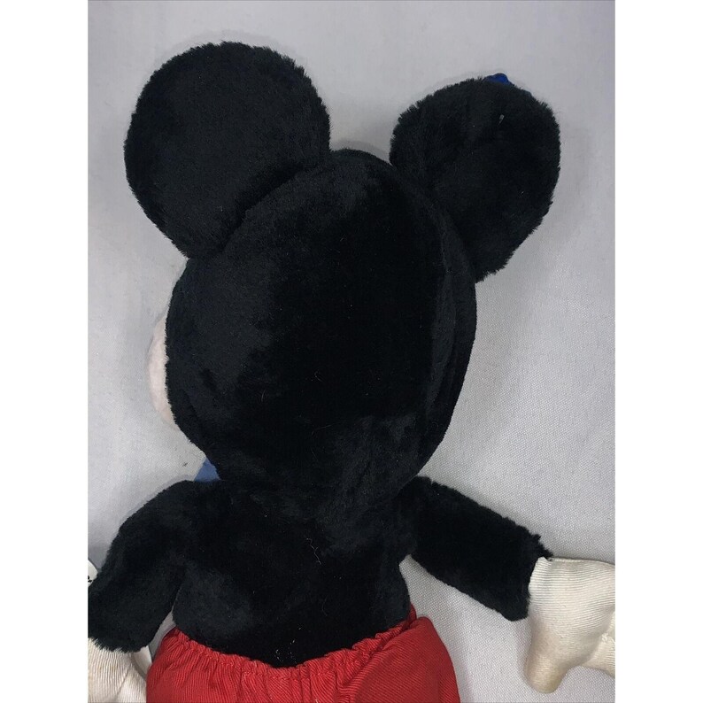 Puede incluir: Juguete de peluche Mickey Mouse negro y rojo con orejas grandes. El juguete est&aacute; de espaldas a la c&aacute;mara.