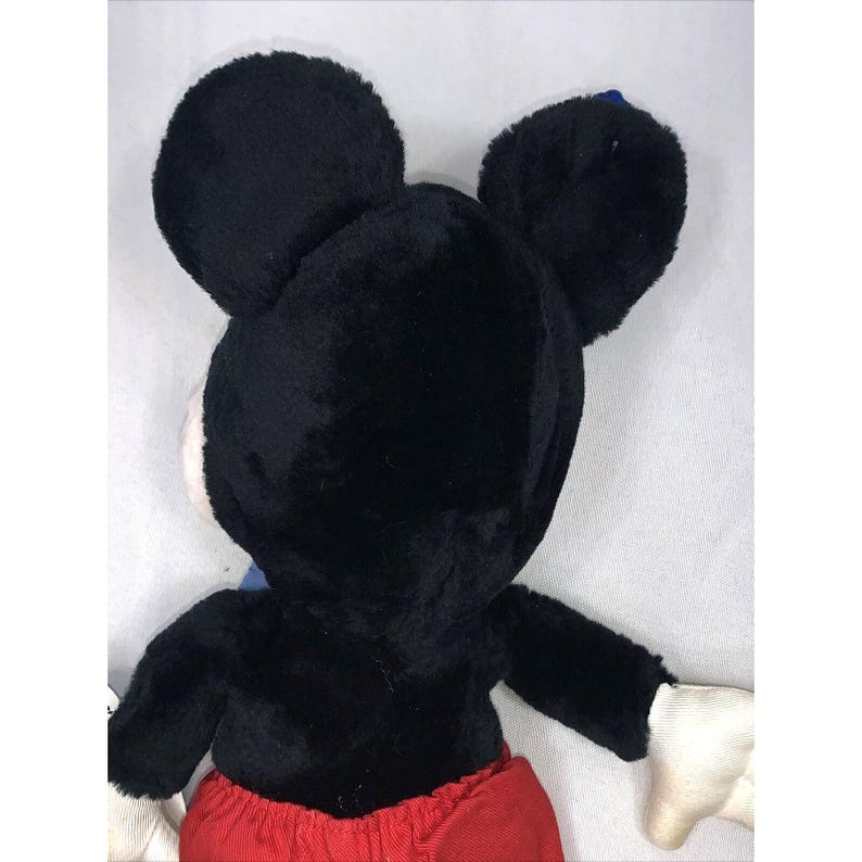 May include: Black plush Mickey Mouse toy with red shorts and white gloves. The toy is facing away from the camera, showing the back of its head.