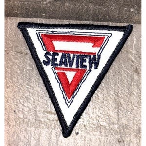 May include: A triangular patch with a white background, a red and white stylized letter "F" and the word "SEAVIEW" in navy blue. The patch is bordered with a black stitched edge.