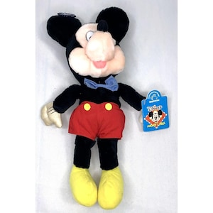 May include: A plush Mickey Mouse toy wearing red shorts, black shoes, and a blue bow tie. The toy has a tag that says "Disney's Mickey Mouse".