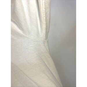 May include: Close-up of a white t-shirt, showing the neckline and shoulder seam. The fabric appears to be a soft, knit material. The lighting is bright, highlighting the texture and construction of the garment.