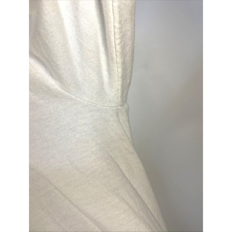 May include: Close-up of a white t-shirt, showing the neckline and shoulder seam. The fabric appears to be a soft, knit material. The lighting is bright, highlighting the texture and construction of the garment.