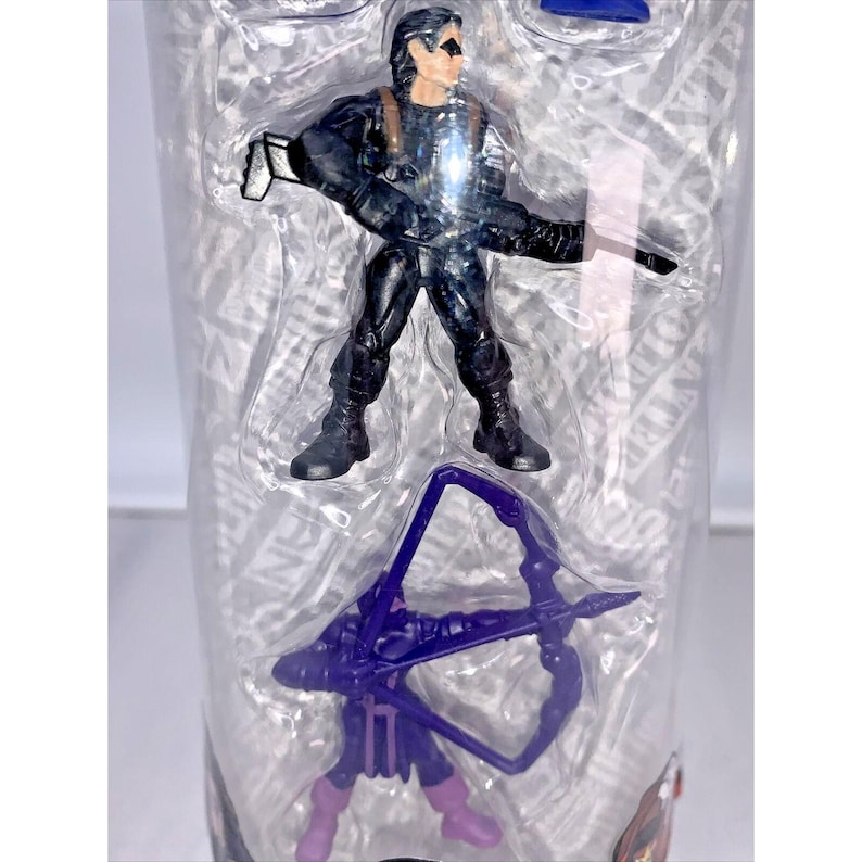 May include: A clear plastic container with a purple bow and arrow, and a black action figure of a superhero with a gun.