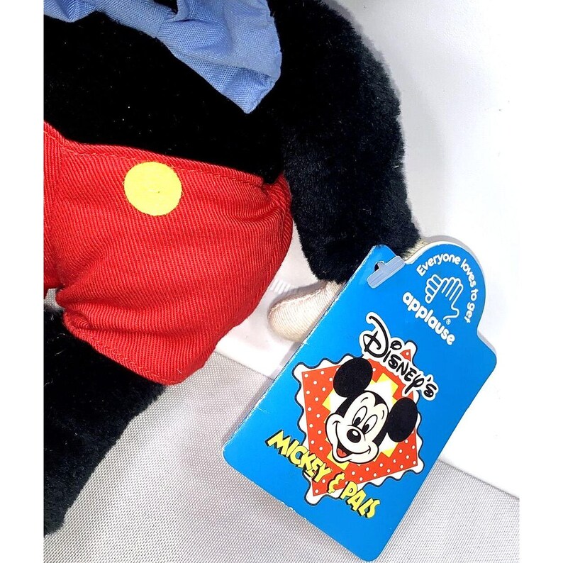 May include: A black and red plush Mickey Mouse toy with a blue bow tie. The toy is holding a tag that says "Disney's Mickey & Pals" and "Everyone loves to get applause".