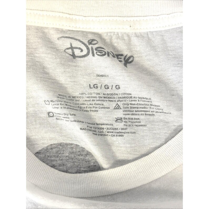 May include: White t-shirt with a gray Disney logo at the top. The shirt's label includes size information, washing instructions, and the text "100% COTTON". The shirt is made in Mexico.