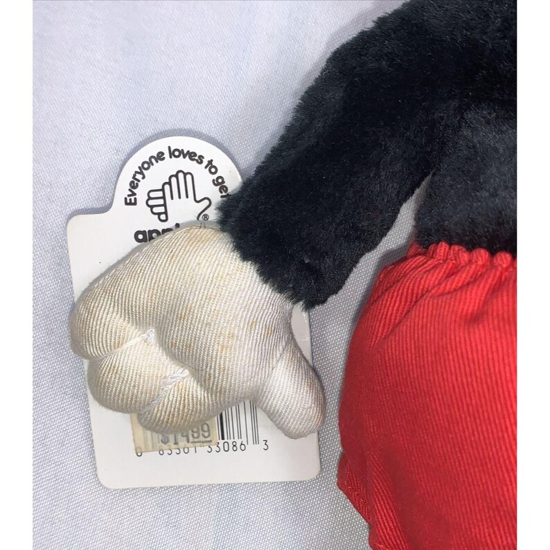 Puede incluir: Juguete de peluche negro y rojo con un guante blanco. El juguete tiene una etiqueta que dice "A todo el mundo le encanta llevarse bien".