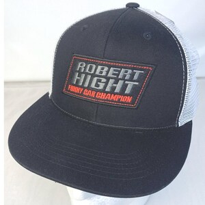 May include: Black and white trucker hat with a red and gray patch that says "Robert Hight Funny Car Champion".