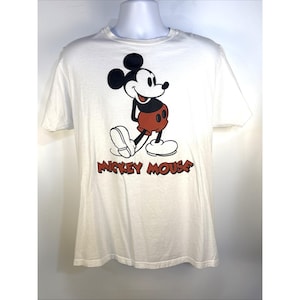 May include: White t-shirt featuring a classic Mickey Mouse graphic. The cartoon character is depicted in black, red, and white, with the words "Mickey Mouse" in red below. A short-sleeved, crew neck tee.