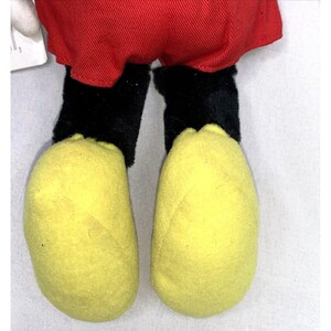 May include: Close-up of a plush Mickey Mouse toy's feet. The feet are yellow with black outlines and are made of soft, fuzzy fabric.