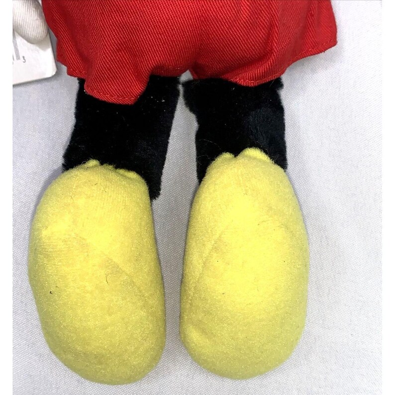 May include: Close-up of a plush Mickey Mouse toy's feet. The feet are yellow with black outlines and are made of soft, fuzzy fabric.