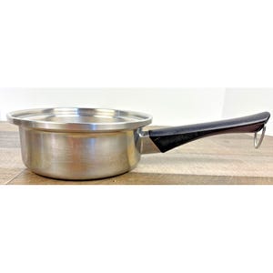 May include: A stainless steel saucepan with a lid and a black handle. The pan has measurement markings on the side and a silver-colored rim. The handle has a loop for hanging.