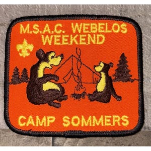May include: Rectangular orange patch with a black border. It features two cartoon bears around a campfire. The text reads "M.S.A.C. Webelos Weekend" and "Camp Sommers" in yellow. A Boy Scout emblem is in the upper left corner.