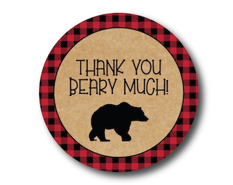 May include: Round thank you sticker with a red and black buffalo plaid pattern. The sticker has a brown background with the text "Thank You Beary Much!" and a black silhouette of a bear.