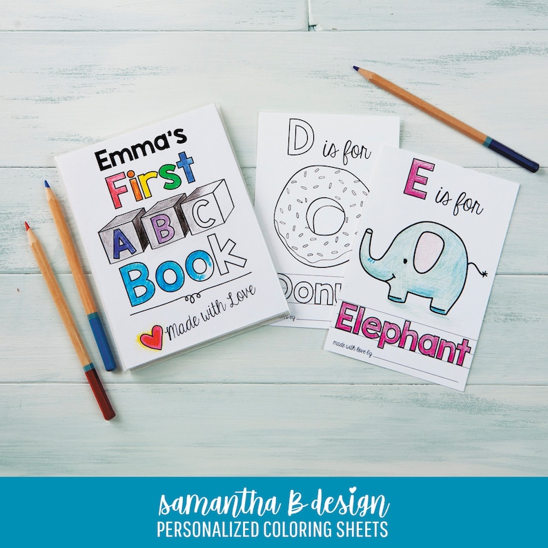 May include: A personalized coloring book titled Emma's First ABC Book with a heart icon, alongside two coloring sheets featuring the letters D for Donut and E for Elephant, accompanied by three colored pencils on a light wooden surface.
