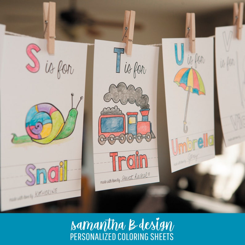 May include: A series of white paper coloring sheets hanging from a string with wooden clothespins. Each sheet features a letter of the alphabet, a hand-colored illustration of a snail, train, or umbrella, and the corresponding word in colorful letters.