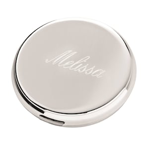 May include: A silver compact mirror with the name "Melissa" elegantly engraved on the lid. The compact is round with a shiny, reflective surface and a small clasp. The overall design is simple and elegant.