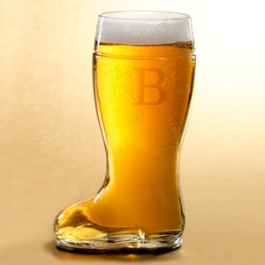 May include: A clear glass beer boot filled with golden beer and topped with white foam. The letter "B" is etched on the glass. The boot-shaped glass is a unique design for beer enthusiasts.