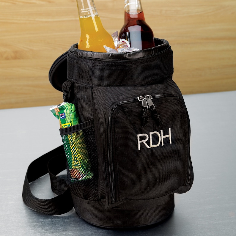 May include: Black insulated beverage cooler bag with a shoulder strap, holding two bottles and ice. Features a front zippered pocket with the embroidered initials "RDH" and a side mesh pocket with a snack. Perfect for picnics or outdoor events.