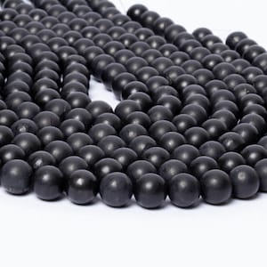 May include: A collection of matte black spherical beads arranged in multiple curved strands. Each bead features a smooth, uniform surface and a consistent dark charcoal colour, creating a dense, textured pattern across the entire display.