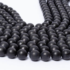 May include: A collection of round, matte black beads arranged in multiple parallel strands. Each bead features a smooth, uniform surface with a consistent dark charcoal colour, creating a dense, textured pattern of spherical shapes across the frame.