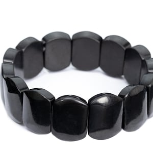 May include: A stretch bracelet composed of multiple smooth, rectangular black beads with rounded edges. The beads are arranged in a continuous circular loop, featuring a polished, reflective surface that catches the light, creating a uniform appearance.
