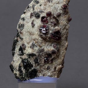 May include: A rough, light-colored rock formation with embedded dark red and black crystals. The rock is labeled "PYROP, CHROMDIOPS Åheim/NO" on a small white tag.