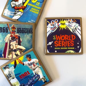 Puede incluir: Cuatro posavasos cuadrados con gráficos de béisbol vintage de los Los Angeles Dodgers. Los diseños incluyen una impresión del décimo aniversario del Dodger Stadium, un programa de la Serie Mundial de 1965, una ilustración de un jugador de 1966 y 1981.
