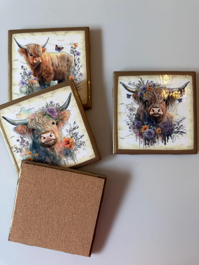 Puede incluir: Un juego de cuatro posavasos cuadrados con ilustraciones de ganado Highland. Tres posavasos muestran retratos detallados de vacas marrones de pelo largo adornadas con coronas florales y mariposas. Un posavasos muestra una parte posterior de corcho.
