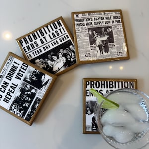 Op de afbeelding: Vier vierkante onderzetters met een glanzende afwerking, elk voorzien van zwart-witte vintage krantenknipsels over het einde van de drooglegging. De koppen luiden PROHIBITION ENDS AT LAST, 14 YEAR DRY ERA OVER en YOU CAN DRINK! REPEAL VOTED.