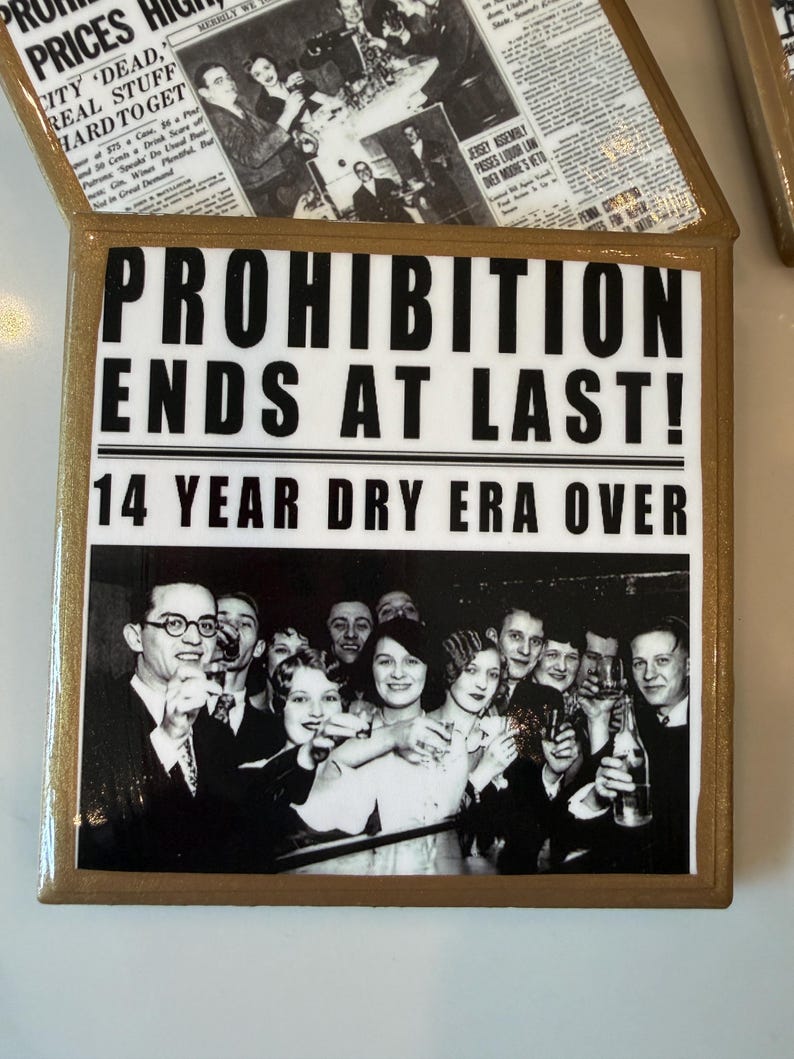 Op de afbeelding: Een vierkante decoratieve tegel met een goudkleurige rand en een zwart-witte afbeelding in krantenstijl. De tekst luidt PROHIBITION ENDS AT LAST! 14 YEAR DRY ERA OVER, vergezeld van een vintage foto van een groep mensen die aan het vieren zijn.