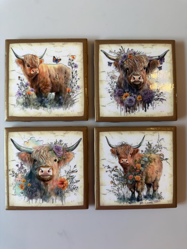 Puede incluir: Un juego de cuatro posavasos cuadrados con ilustraciones de ganado Highland. Cada posavasos muestra una vaca marr&oacute;n de cuernos largos, rodeada de arreglos florales estilo acuarela, vegetaci&oacute;n y mariposas sobre un fondo claro y texturizado.